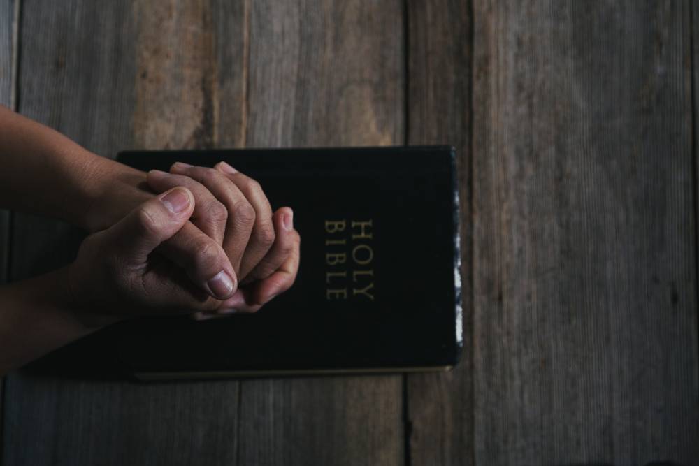 Hands folded in prayer on a Holy Bible in church concept for faith, spirituality and religion, woman praying on holy bible in the morning. woman hand with Bible praying.